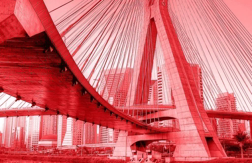 A picture of Sao Paulo from a large cable-stayed bridge with several cables and massive concrete pillars. Tall buildings of a modern skyline can be seen in the background.