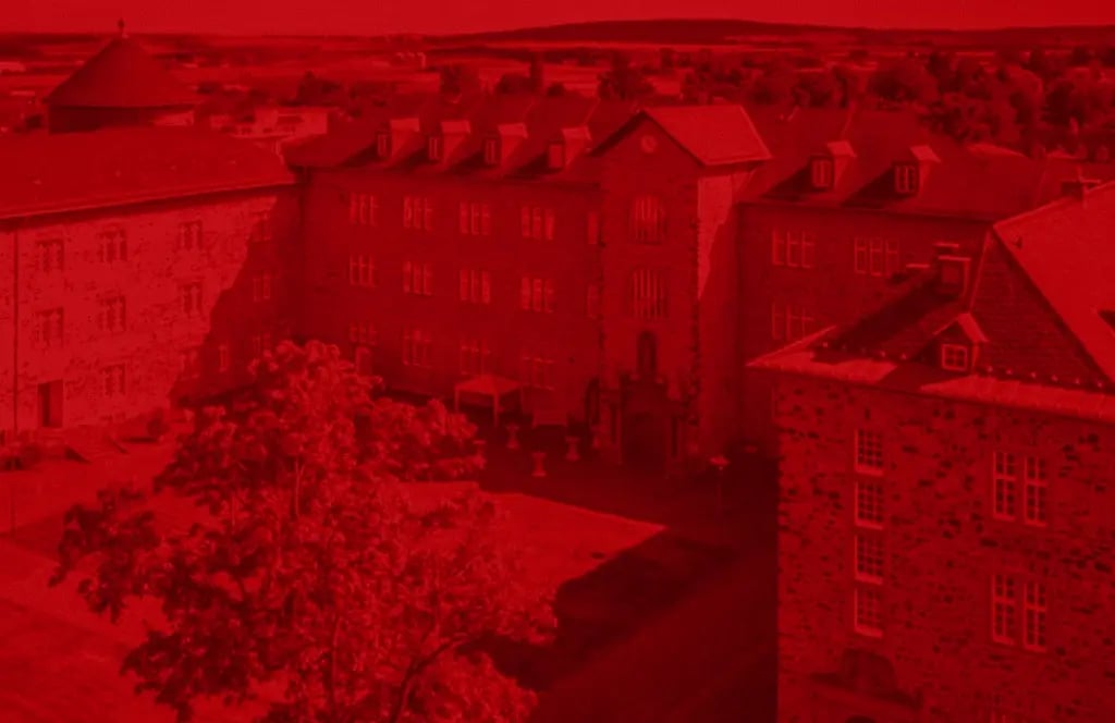 A historic castle building with several wings and an inner courtyard. There are trees in the foreground and a wide landscape is visible in the background.