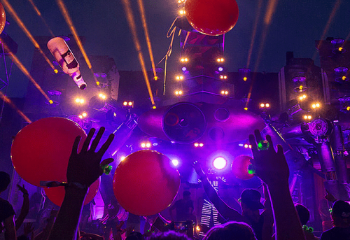 People with red balloons in front of a stage with laser lights and decoration, at a live event or music festival.