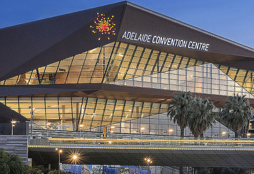 Exterior view of the Adelaide Convention Center with modern glass façade and striking architecture, palm trees and street in the foreground.
