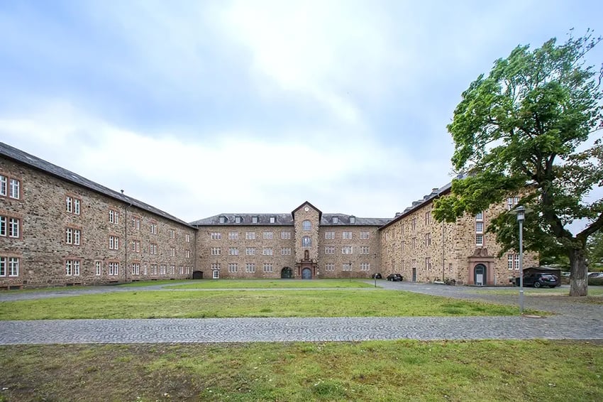 Schloss Butzbach ein historisches Gebäude aus Stein mit Innenhof und Grünfläche. Symmetrische Fassade, mehrere Fensterreihen, Baum rechts im Vordergrund, gepflasterter Weg. Hauptbüro von RIEDEL Networks